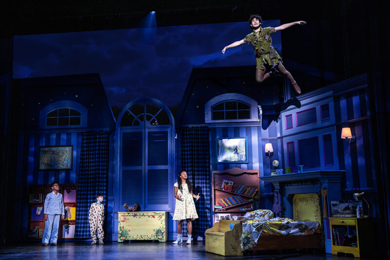 Micah Turner Lee as John, Reed Epley as Michael, Hawa Kamara as Wendy, and Nolan Almeida as Peter Pan in Peter Pan. The Darling’s, all in pjs, look up at Peter as he flies around the room.